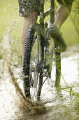 Mountainbiker passing dirty puddle, Upper Bavaria, Germany
