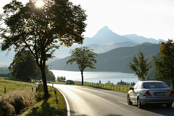 Car driving on alpine road at lake Weissensee near Fussen, Swabia, Bavaria, Germany