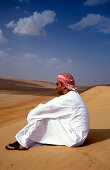 Mann sitzt im Sand in der Wüste, Sultanat Oman, Vorderasien, Asien