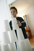 Junge baut einen Turm aus Plastikbechern