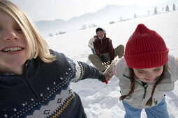 Children pulling parents in toboggan on snow, side view