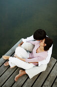 Couple sitting on jetty, man with arms around woman