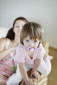 Mother and daughter with pacifier sitting on cane chair