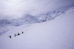 Four people with skies and snowboard walking up a snowcapped mountain, Kuehtai, Tyrol, Austria