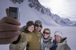 Four young skier taking a picture of themselves with a camera phone, Kuehtai, Tyrol, Austria