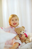 Toddler girl holding her teddy in bedroom