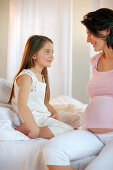 Mother and daughter sitting on bed, smiling