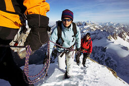 Eine Frau und ein Mann am Seil eines Bergführers wandern über einen exponierten Schneegrat. Titlisgipfel, Zentralsschweiz, Schweiz, Alpen, Europa, MR