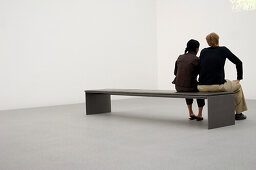 Couple sitting on bench in museum, Pinakothek der Moderne Munich, Bavaria, Germany