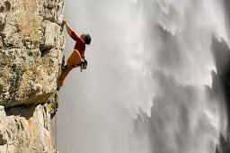 Woman climbing up rock face in front of waterfall, Carinthia, Austria