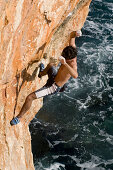 Man climbing on rock face over water, Majorca, Spain