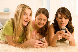 Teenage girls (14-16) on bed using mobil phones