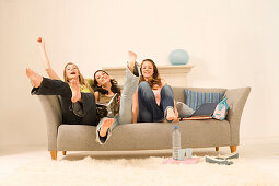 Teenage girls (14-16) sitting on sofa stretching legs high