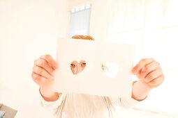 Teenage girl (14-16) holding sheet with hearts in front of face