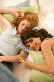Two teenage girls (14-16) snuggling together on bed, listening to portable MP3 player