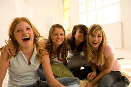 Four teenage girls (14-16) having fun, sitting on floor, indoor