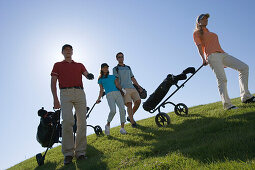 Group of people walking on golf course pulling golf bag on wheels, sideview, Apulia, Italy