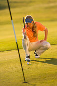 Female golfer lining up ball on putting green, Apulia, Italy