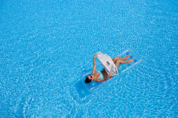 Woman reading newspaper on air mattress in pool, Apulia, Italy