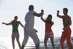 Junge Leute mit Animateur bewegen sich am Strand, Apulien, Italien