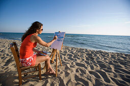 Young woman painting picture on beach, Apulia, Italy