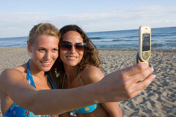Two young woman on beach, taking picture with camera phone, Apulia, Italy