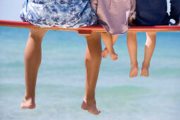 Junger Mann und zwei Kinder sitzen auf einer Bank am Strand, Apulien, Italien