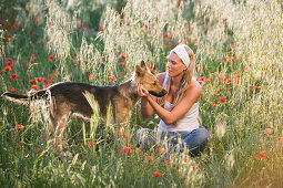 Young woman sitting in flower meadow, stroking a dog, Apulia, Italy