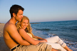 Young couple sitting on beach, sea shore, Apulia, Italy