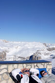 Touristen sonnen sich vor schneebedeckter Landschaft, Passo Pordoi, Dolomiten, Iitalien, Europa