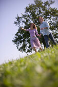 Couple running down on meadow holding hands