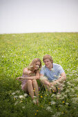 Young couple sitting on meadow, woman pointing