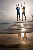 Two people jumping on jetty, arms raised
