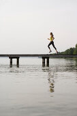 Junge Frau joggt auf einem Steg am See