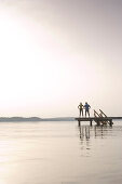 Two people standing on jetty, looking over lake