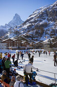 People curling on a rink, Matterhorn in background, Zermatt, Valais, Switzerland (Curling: A rink game where round stones are propelled by hand on ice towards a tee (target) in the middle of a house (circle)).