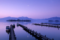 Landing stage and boats at dawn in Gstadt at lake Chiemsee with Fraueninsel, Hochplatte, Hochgern and Hochfelln in the background, Chiemgau, Upper Bavaria, Bavaria, Germany