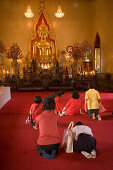 People praying in front of a gilded Buddha statue, Wat Suthat, Bangkok, Thailand