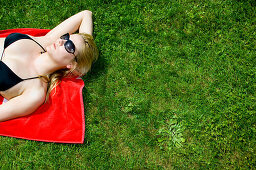 Young woman sunbathing, lying on grass, wearing black bikini top, Starnberger See, Upper Bavaria, Germany