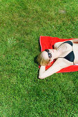 Young woman lying on grass, listening to MP3 player, Starnberger See, Upper Bavaria, Germany