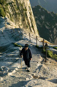 daoist monk on Fish Back Ridge, approaching Cui Yun Gong Monastery on South Peak, pilgrim path along stone steps with chain handrail, cliffs of West Peak, Hua Shan, Shaanxi province, Taoist mountain, China, Asia