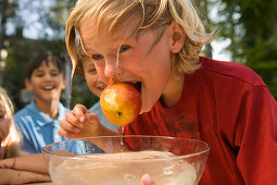 Boy with wet hair holding an apple in his mouth, dish wath water in front of him, children's birthday