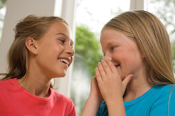 Girl whispering into girlfriend's ear, children's birthday party