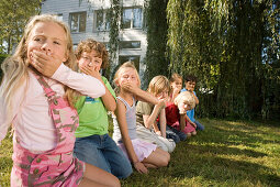 Kinder hocken auf einer Wiese und machen Grimasse in die Kamera, Kindergeburtstag