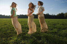 Three children having a sack race, children's birthday party