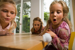 Drei Mädchen spielen Wattebausch blasen, Kindergeburtstag