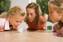 Drei Mädchen spielen Wattebausch blasen, Kindergeburtstag