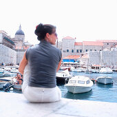 Female tourist sitting at harbour near city wall, Dubrovnik, Dalmatia, Croatia
