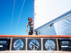 Mann steht auf Segelboot und befestigt Segel, Instrumententafel im Vordergrund, Kieler Bucht zwischen Deutschland und Dänemark