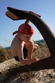 Junge spielt Pirat an einem rostigen Anker am Strand, Ilha de Tavira, Tavira, Algarve, Portugal